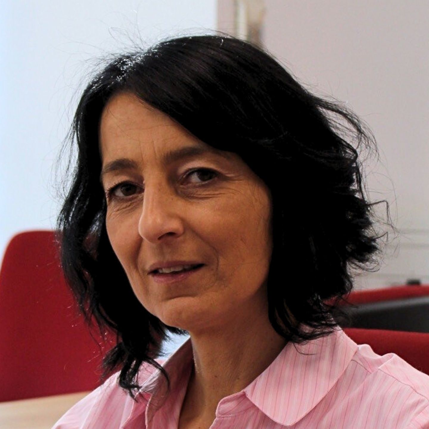 Cristina Pasere, Gestora de Suporte às Operações de Conformidade da EOS Roménia, está sentada na sua secretária com uma blusa às riscas cor-de-rosa e a olhar para a câmara.