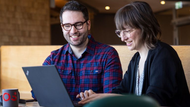 Dois colaboradores da EOS olham para um laptop juntos enquanto estão absortos em uma conversa.