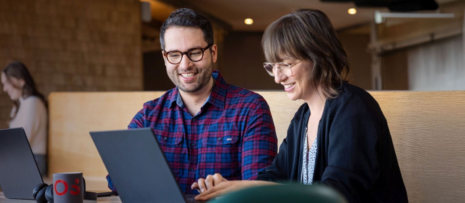 Dois colaboradores da EOS olham para um laptop juntos enquanto estão absortos em uma conversa.
