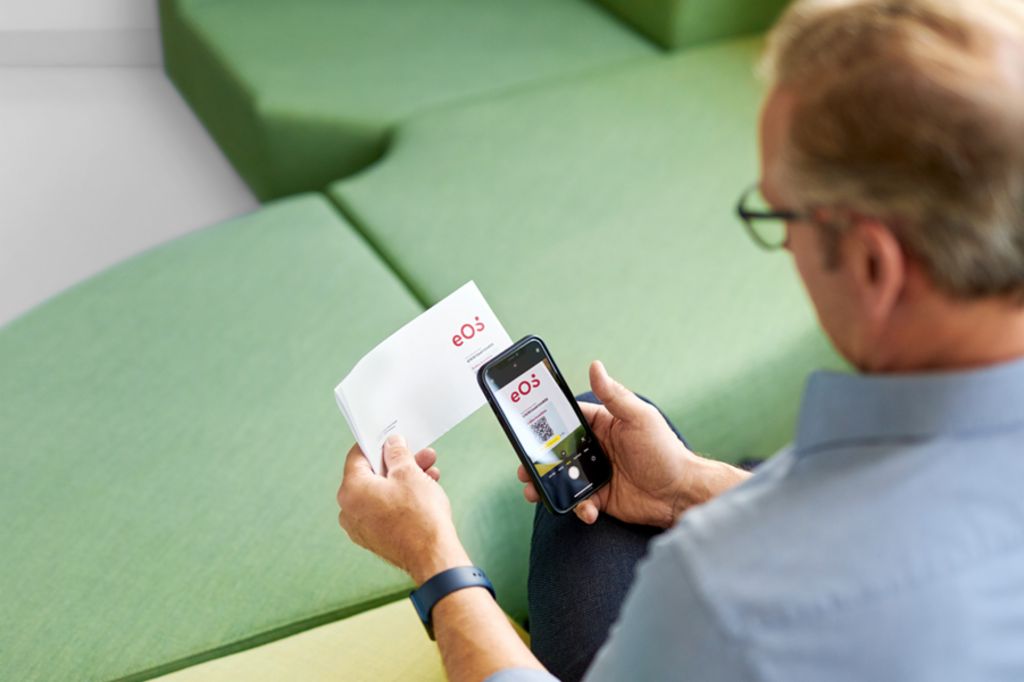 Um homem escaneia um código QR em uma carta da EOS com seu smartphone para pagar sua reivindicação em aberto online no Portal EOS.