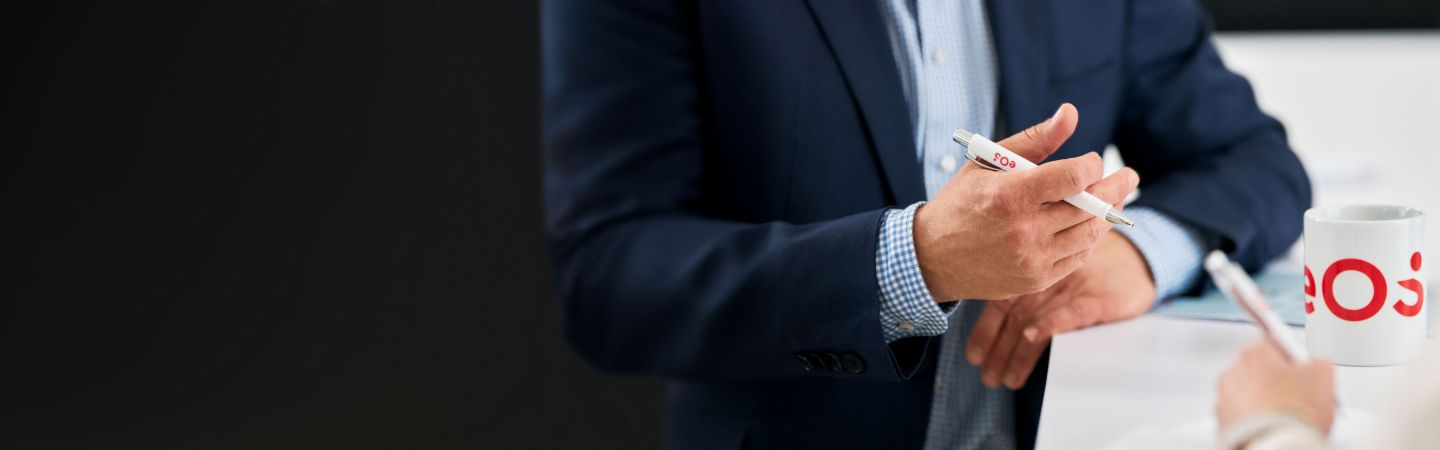 Empresário segurando uma caneta EOS durante uma conversa sobre gestão internacional de recebíveis, xícara EOS na mesa - Especialização em cobrança de dívidas, NPLs e soluções digitais