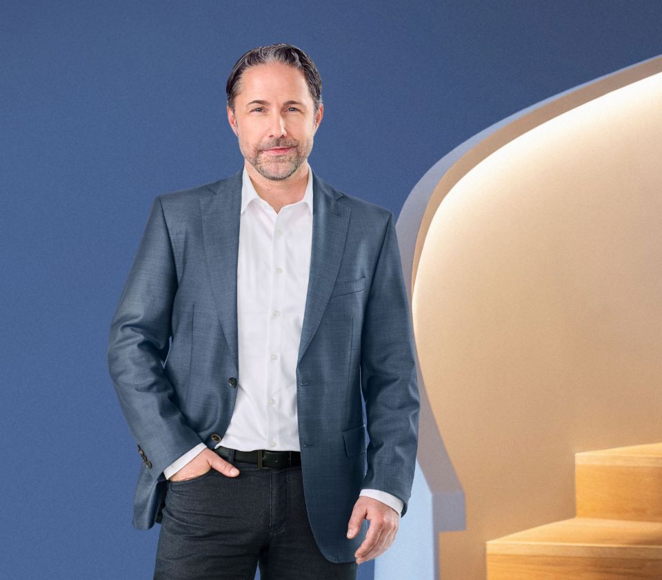Marwin Ramcke, Diretor Executivo do Grupo EOS, está em frente a um fundo azul, vestido com um casaco escuro. Ele olha diretamente para a câmera.