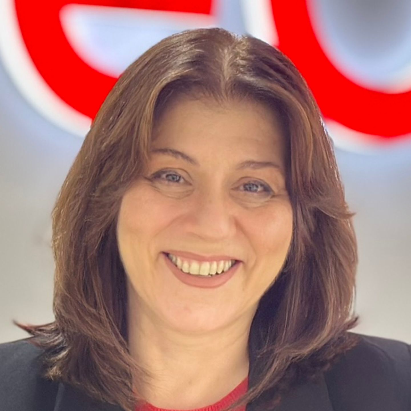 Belén Barreiro, agente de contact center da EOS em Espanha, está encostado a um balcão com um blazer preto em frente a um logótipo brilhante da EOS.