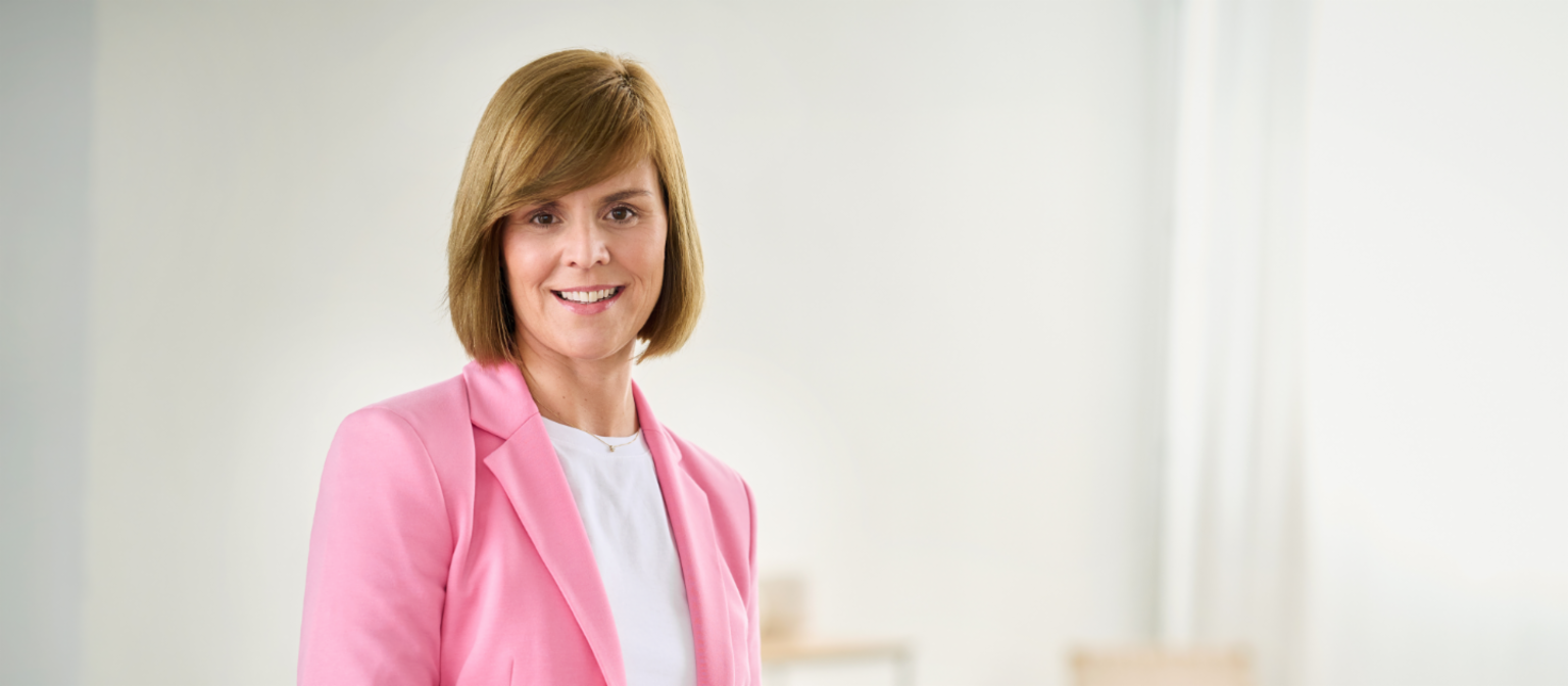 Eva Griewel está numa sala iluminada e veste um blazer cor-de-rosa com uma camisa branca