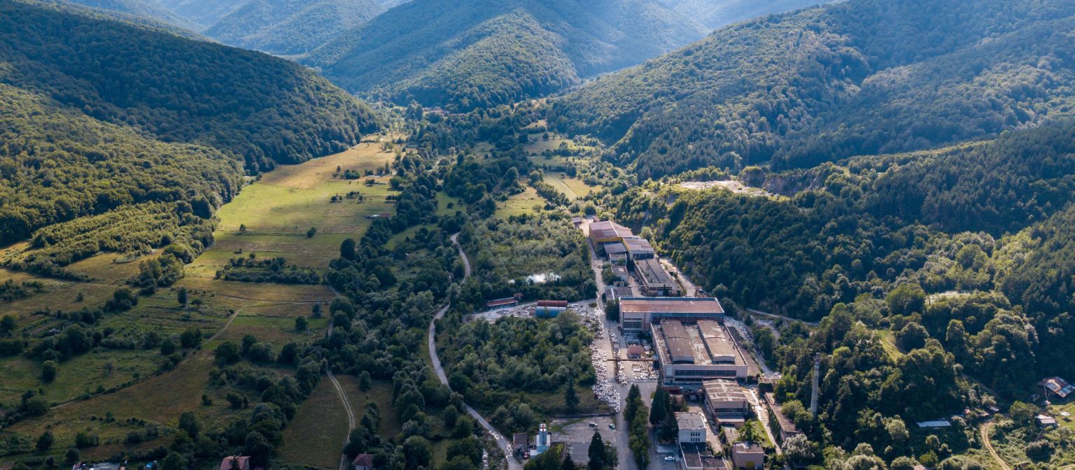 Gestão de recebíveis: A imagem mostra uma vista aérea da fábrica de mármore em Berkovitsa, rodeada por muitas árvores num vale. Devido ao empenho da EOS, a empresa tradicional foi preservada.