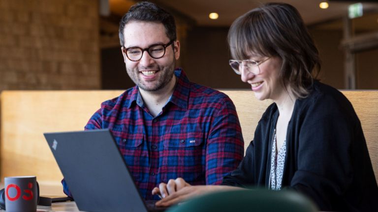 Dois colaboradores da EOS olham para um laptop juntos enquanto estão absortos em uma conversa.
