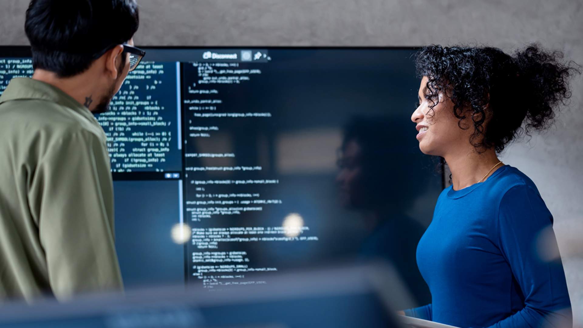 IA na recuperação de dívidas: Nesta imagem, dois profissionais estão analisando colaborativamente o código do programa para processos automatizados em uma grande tela. A cena ilustra a aplicação prática da Inteligência Artificial (IA) e da Automação de Processos Robóticos (RPA) na gestão de dívidas — um exemplo de transformação digital na gestão de recebíveis.